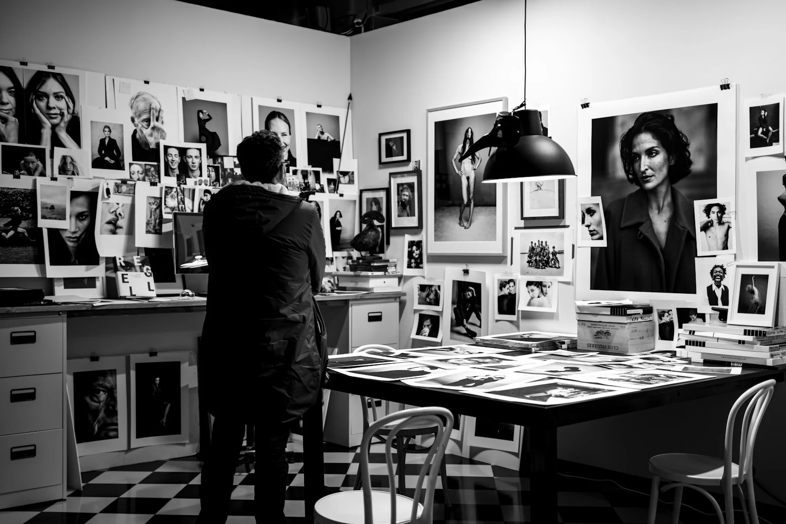 Photographer examining a gallery wall of portrait prints in a photography studio