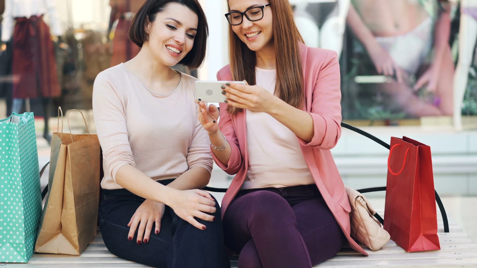 Two women friends looking at a phone together — the word-of-mouth moment that referral marketing for photographers is built to capture